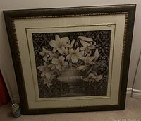 Full view of framed painting depicting white lilies in a bowl on patterned background, showing overall condition and scale with soda can for reference.
