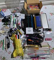 Full lot with pens, pencils, correction tapes, washi tape rolls, markers, and other stationery items spread across a floral tablecloth surface.