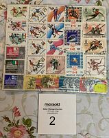 Photo showing a sheet of used Magyar Posta postage stamps featuring various athletes in different sports such as ice skating, skiing, basketball, and boxing with visible cancellation marks.