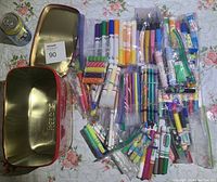 Overview of assorted markers, crayons, erasers, colored pencils, pens, and metal tins on floral tablecloth