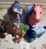 Top view of six My Little Pony doll figures including large and small ponies with various hair colors and accessories, arranged on a patterned surface.