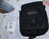 Photo of black Onepolar camera bag showing front flap closed with a plastic buckle, various zipper compartments visible.