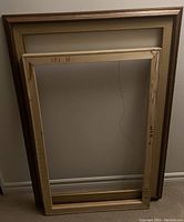 Three empty wooden painting frames stacked inside each other, showing front and backing wooden stretchers with visible wear and corner damage