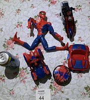 Full view of all 5 Spider-Man toys arranged on floral background, includes large Spider-Man figure, spider-themed vehicle, car, motorcycle, and round container.