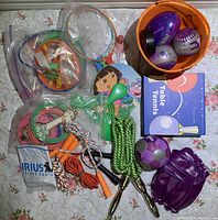 Overview of sporting goods lot including baseballs, glove, jump ropes, rings, and table tennis items laid out on floral fabric