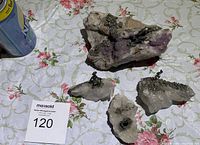 Four stones with quartz and amethyst crystals on a floral tablecloth with attached small metal animal figures resembling dogs.