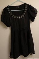 Front view of black dress with puff sleeves and decorated neckline.