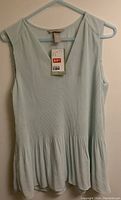Front view of light blue sleeveless women's dress hanging on a hanger, showing its V-neck and gathered lower hem