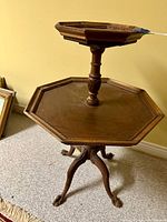 View of octagonal two-tier mahogany table showing the overall structure, carved pedestal column, and claw foot tripod base on carpet.