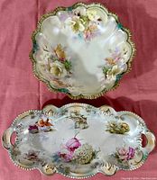 Top-down view of the two porcelain pieces on a pink fabric, showing bowl with large floral blossoms and celery dish with multiple floral groupings and gold details