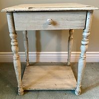 Front full view of antique white painted wooden side table showing drawer and turned legs.