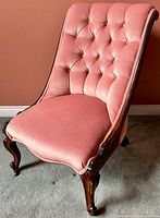 Side angled view of Victorian slipper chair showing pink upholstery and carved wooden legs.