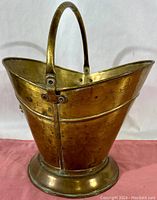 Front left angled view showing the brass coal scuttle bucket with curved handle, wide mouth, and rounded base.
