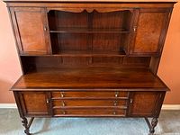 Front view of the antique mahogany Welsh dresser showing upper cabinets with two doors and open shelves, and lower section with three drawers flanked by two cabinet doors, standing on turned legs.