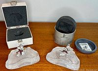 Two Swarovski crystal Kris Bear figurines on clear textured bases, with original boxes, displayed on wooden surface.