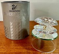Swarovski branded packaging next to the crystal clam shell figurine with pearl sitting on a wooden surface.