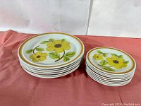 Image shows two stacks of Royal Doulton plates on a pink cloth background, larger plates on left and smaller on right, all with yellow floral design and double band rim