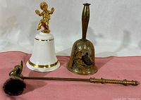 Porcelain cherub bell, brass bell, and brass candle snuffer together on display