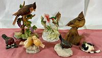 Seven various ceramic bird figurines arranged on pink cloth background.
