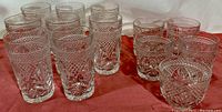 Complete set of 17 vintage pressed glass tumblers arranged on a red cloth showing various sizes and cut glass patterns.