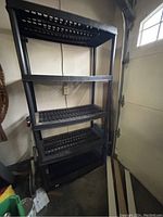 Photo of black plastic shelving unit with five shelves in a garage setting.