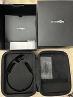 Open black travel case with foam insert shaped to fit the headset, alongside the AfterShokz branded box and paperwork.