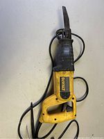 Front view of the DeWalt reciprocating saw showing yellow and black body, attached blade, and power cord coiled beside it.