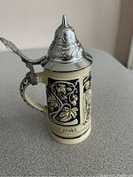 Side view of the German beer stein showing grapevine relief design and pewter lid with thumb lever.