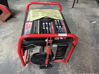 Front–top perspective showing full unit with red frame, black fuel tank, and operator manual on top.