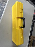 Closed yellow hard plastic carrying case with black handle shown from the top