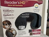 Packaging front showing Reader's HD OttLite LED Illumination neck pillow with features like memory foam, low glare light, and interchangeable covers.