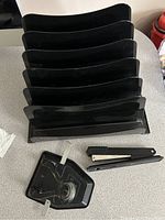 Photo showing a black file organizer with multiple tiers, a black stapler, and a black two-hole punch laid out on a gray surface.