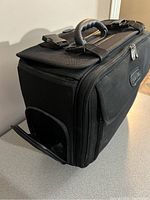 Side view of the black roller briefcase showing wheels, handle, and zippered compartments