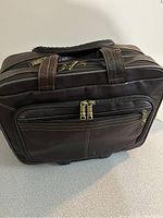 Front view of the brown Samsonite roller briefcase showing multiple zippered compartments and two top handles with a leather wrap grip.