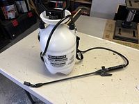 Full view of white plastic spray applicator with hose and wand on table.