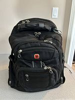 Front and top view of black Swiss Gear backpack with multiple compartments and logo visible.