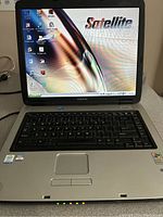 Front view of Toshiba Satellite A60 laptop powered on showing desktop screen with Satellite logo and functional keyboard and touchpad.