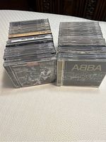 Two stacks of assorted CDs in plastic jewel cases, showing ABBA CD on top of one stack and a black and white cover on the other.