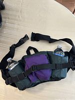 Top view of the water fanny pack on table, showing two water bottles in side pockets, purple central pouch, and adjustable straps.