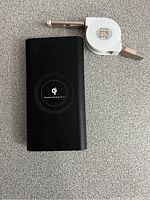 Top view of black rectangular power bank showing Qi wireless charging pad and retractable white USB cable.