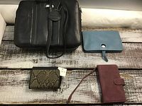 Two purses on a wooden surface. One is black leather Jessica brand and the other is blue leather Hermes with a button clasp.