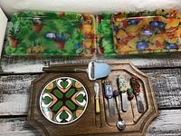 View of cheese board and spreaders with two colorful plastic trays behind