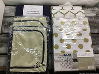 Photo showing seven cloth storage boxes wrapped in plastic, navy blue cube bins and patterned white bins with gold accents.