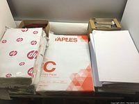 Pack of HP branded 11x17 copy paper and Staples branded 8.5x14 copy paper sheets stacked with two boxes of coin wrappers on top.