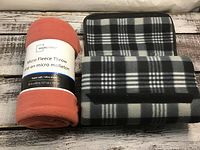 Rolled rust-colored fleece throw and folded gray and black plaid fleece throw on a wooden surface
