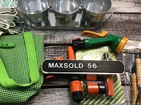Photo showing green mesh garden tool bag, garden gloves, metal pots in tray, and garden hose accessories
