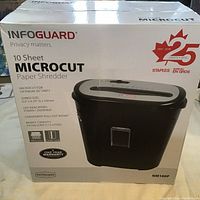 Front view of the Infoguard paper shredder box showing product features including 10 sheet capacity, microcut shred size, LED indicators, pull-out basket with 3 gallon capacity, and one year warranty.
