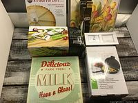 Photo showing all items in the lot including the pie divider, mandolin, milk sign, egg poacher, clock, and placemats