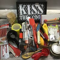 Overview of kitchen utensils and tools including spatulas, whisks, peelers, measuring tools, and decorative sign.