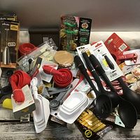 Photo taken showing an assortment of new and lightly used kitchen utensils and tools including measuring cups, spoons, ladles, marinade injector, whisk, and kitchen gadgets.